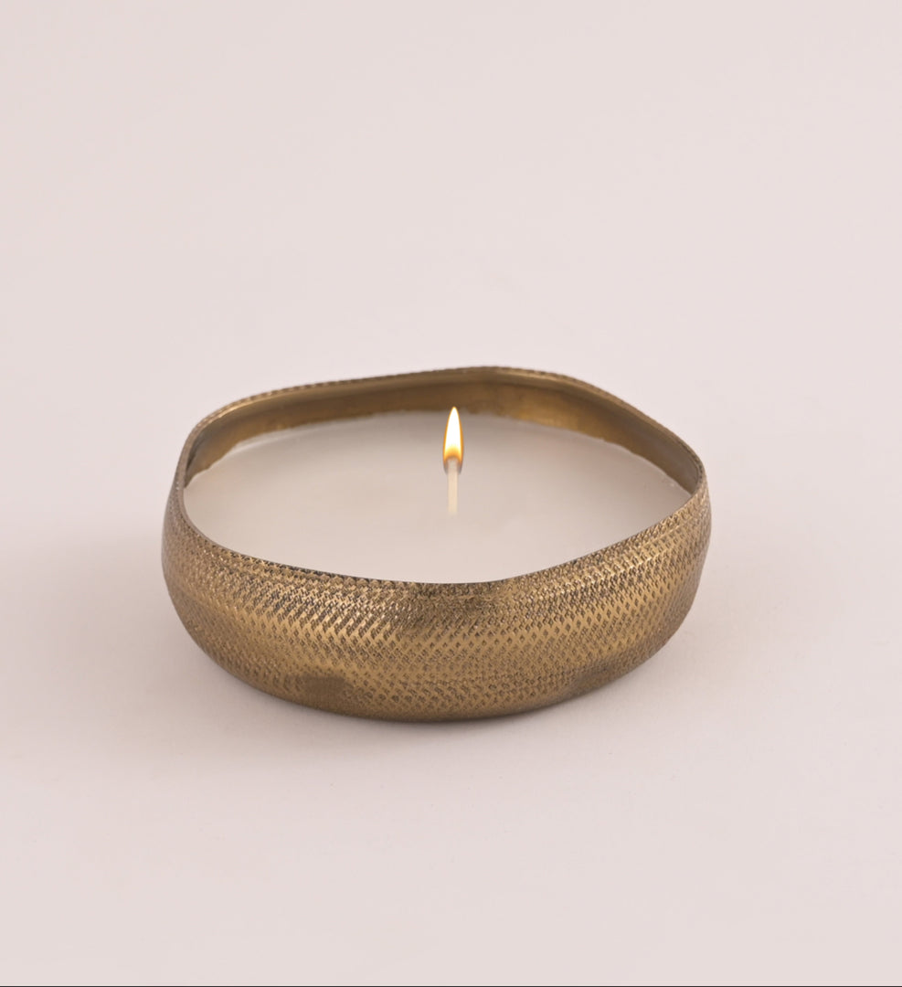 Brass candle holder with a lit candle on a light beige background